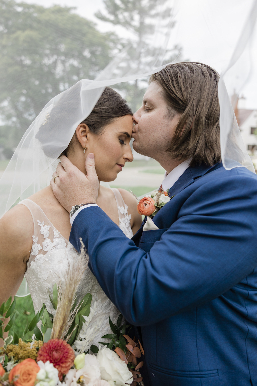 Groom plants a kiss on the bride's forehead under her sheer veil as she closes her eyes, captured by Michigan wedding photographer Holly Kattlegreen