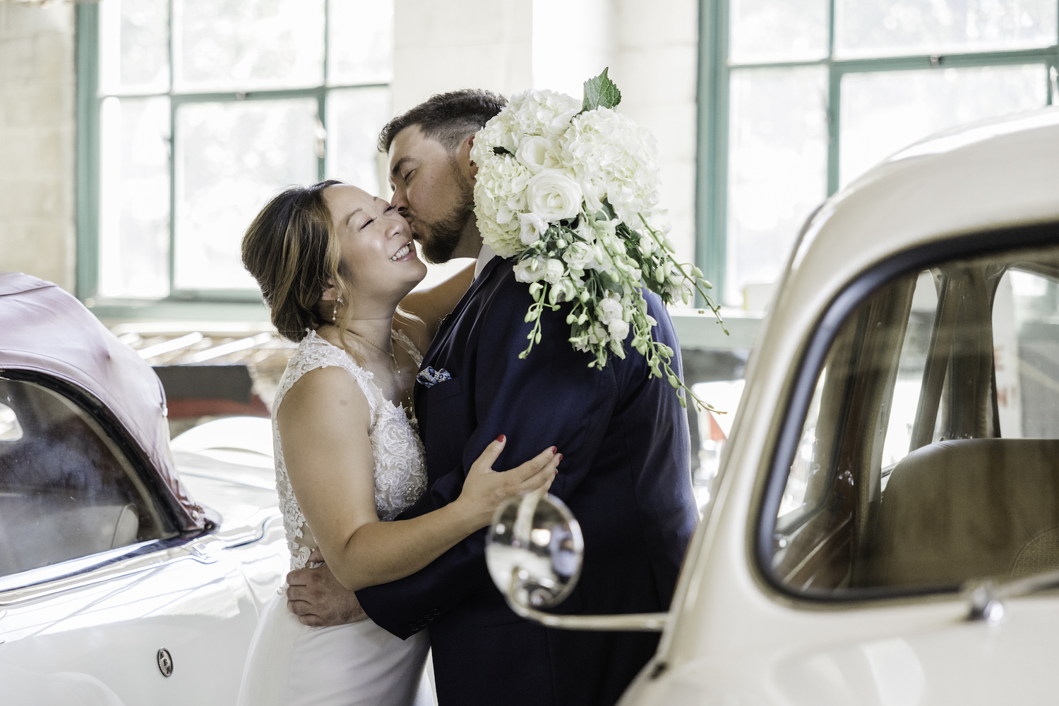 Newlywed couple sharing an embrace as they groom plants a kiss on the bride's cheek while she smiles, captured by Holly Green Photography